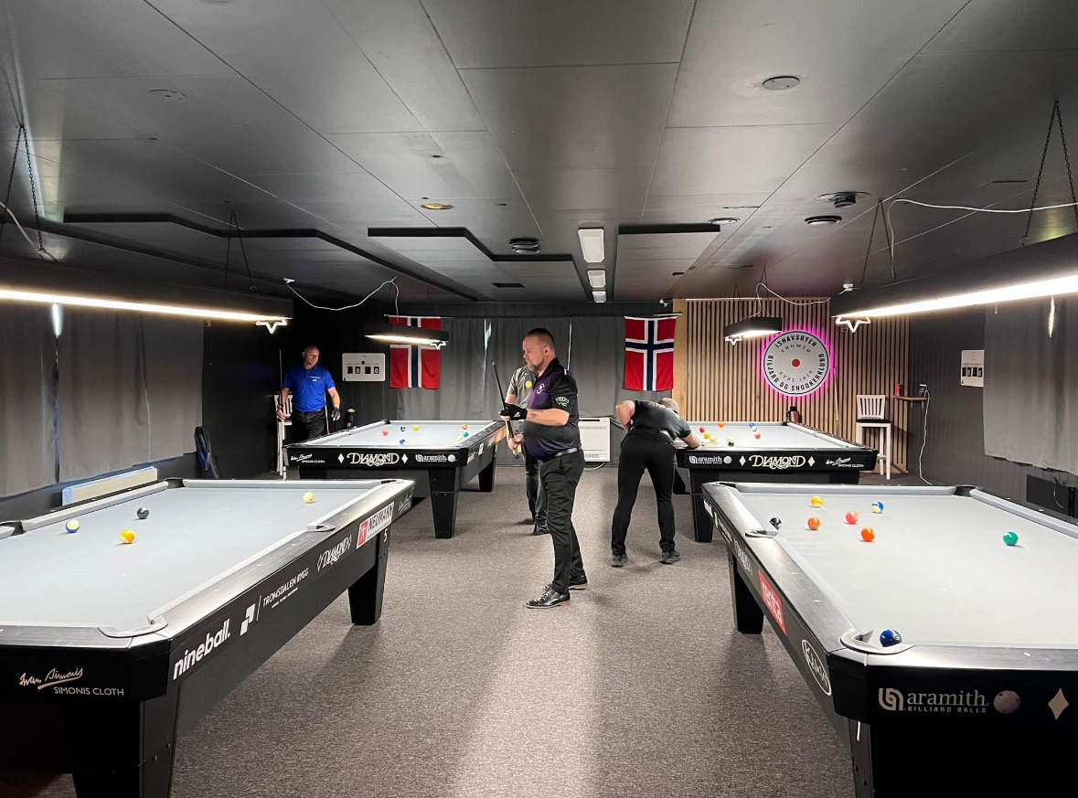 Snookerlokalet med tre spillere og norske flagg på bakveggen